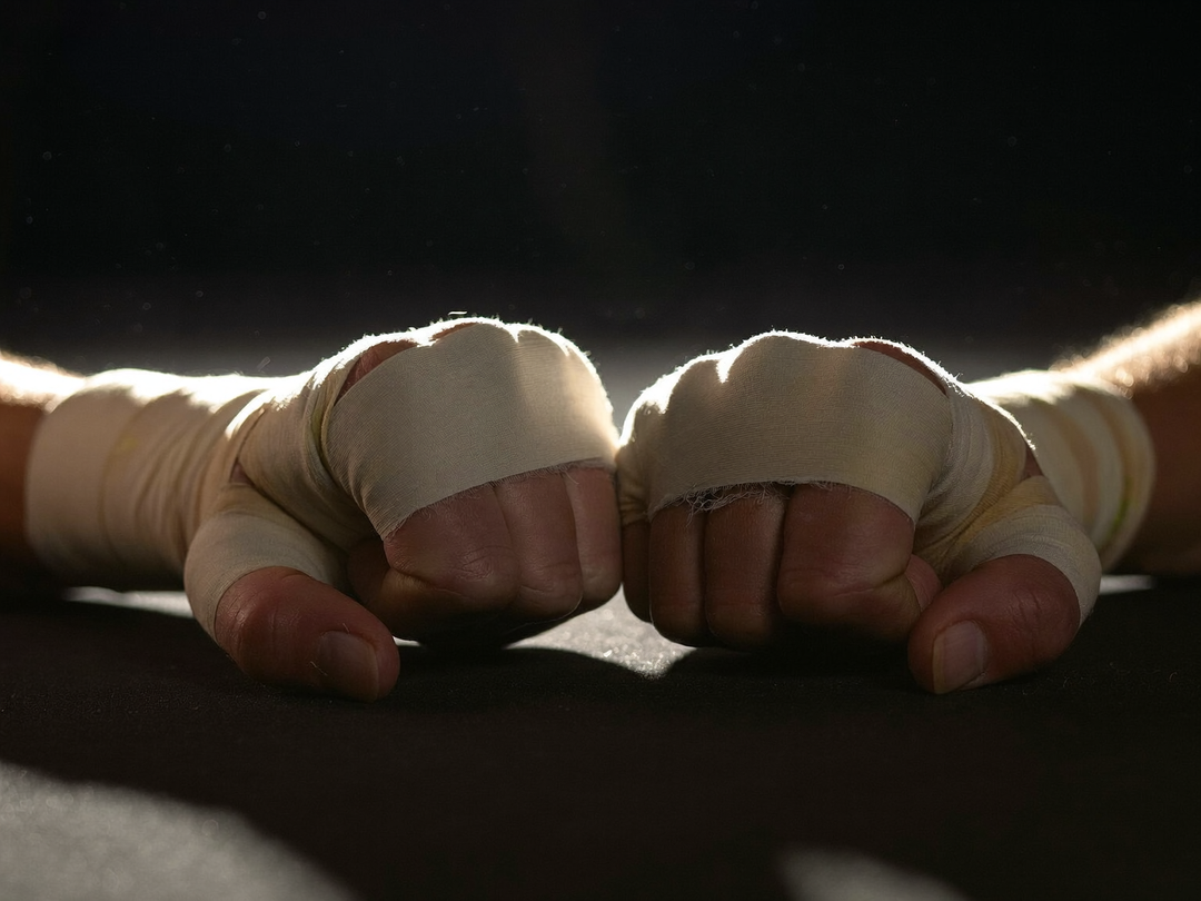 Gros plan sur deux poings bandés posés sur le tapis sombre après un combat, contre-jour
